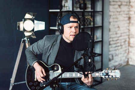 Close up of a man singer in a headphones with a guitar recording a track in a home studio. Man...