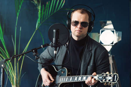 Close up of a man singer sitting on a stool in a headphones with a guitar recording a track in a...