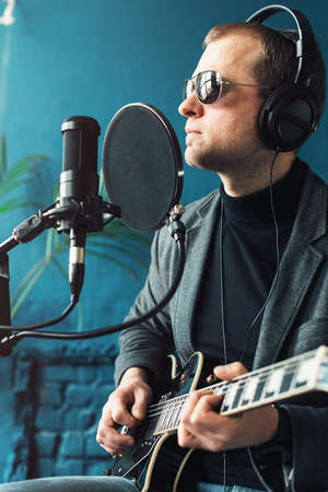 Close up of a man singer sitting on a stool in a headphones with a guitar recording a track in a home studioの写真素材