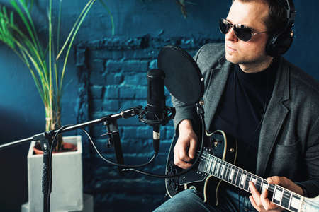 Close up of a man singer sitting on a stool in a headphones with a guitar recording a track in a...