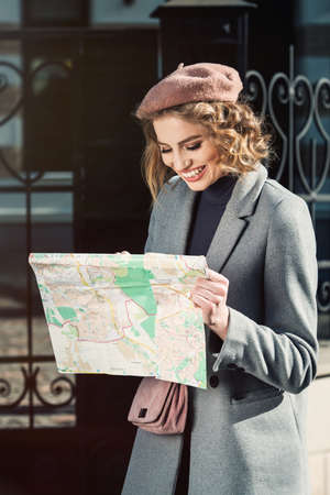 Cute young beautiful curly smiling caucasian travelling woman reading a map.の写真素材