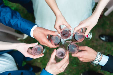 People hold in hands glasses with red wine. wedding party. friends toasting with a champagne above white tableの写真素材