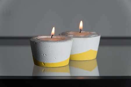 Two candles in white and yellow concrete candle holders.の写真素材