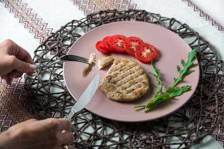 woman eats juicy fried meat cutlet with tomato on a plate.の写真素材