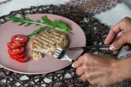 woman eats juicy fried meat cutlet with tomato on a plate.の写真素材