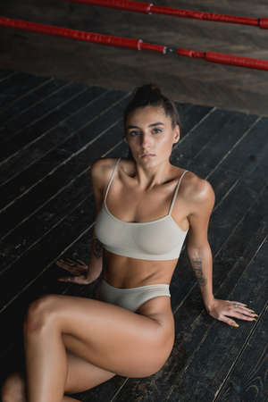 Fashionable brunette girl in a biege underwear posing on a floor in a boxing ringの写真素材