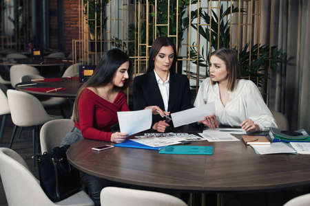Business women in smart casual wear are discussing affairs, drinking coffee and smiling while co-working in the cafeの写真素材