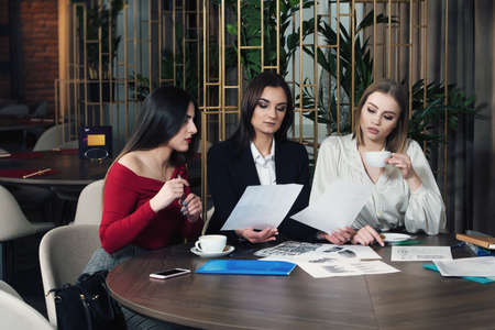 Business women in smart casual wear are discussing affairs, drinking coffee and smiling while co-working in the cafeの写真素材