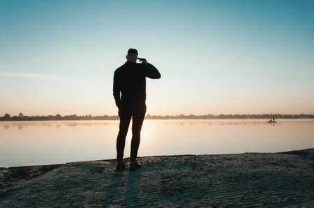 Suicide minds. silhouette of depressed young man holding gun near his head standing near water.の写真素材