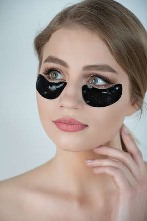 Under Eye Skin Black Patch. Closeup Of Beautiful Young Woman Face With Moisturizing Collagen Mask Pad On Healthy Fresh Facial Skin On White Background. High Resolution.の写真素材