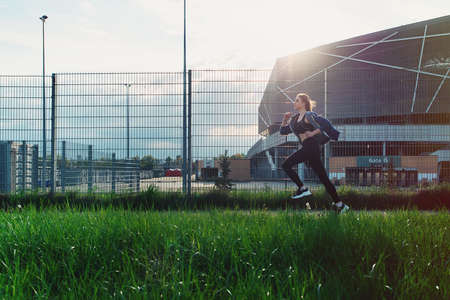 Young attractive female running on sunset in city with earphones listening to music during training.の写真素材