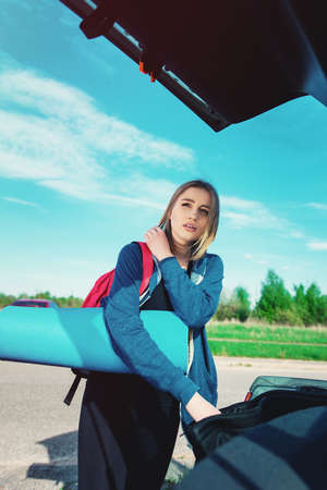 Young woman carrying blue yoga mat and putting it into a car trunk. preparation for trainingの写真素材