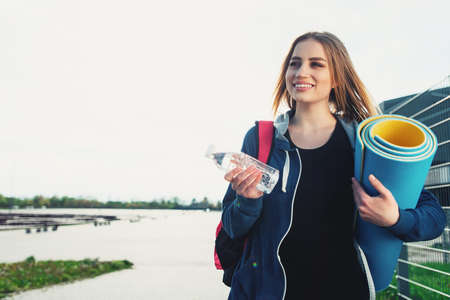 Young girl with a bottle of water and gym mat outdoors.の写真素材