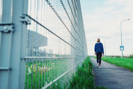 Sad Thoughtful teenage hipster girl standing alone in front of the metal grid .の写真素材