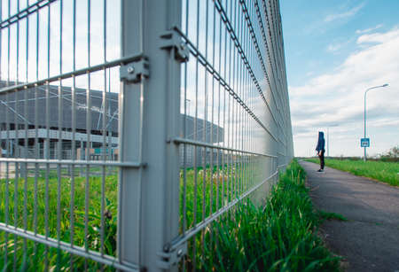 Sad Thoughtful teenage hipster girl standing alone in front of the metal grid .の写真素材