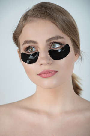 Under Eye Skin Black Patch. Closeup Of Beautiful Young Woman Face With Moisturizing Collagen Mask Pad On Healthy Fresh Facial Skin On White Background. High Resolution.の写真素材