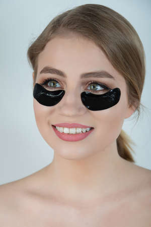 Under Eye Skin Black Patch. Closeup Of Beautiful Young Woman Face With Moisturizing Collagen Mask Pad On Healthy Fresh Facial Skin On White Background. High Resolution.の写真素材