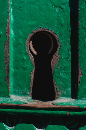 A rusty keyhole in an old cracky green metal door .