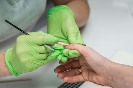 Professional manicure master in green gloves making manicure in salon. Nails treatment in SPA salon....