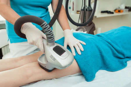 Cropped shot of a professional dermatologist in white gloves performing radiofrequency lifting procedure on the stomach of a womanの写真素材