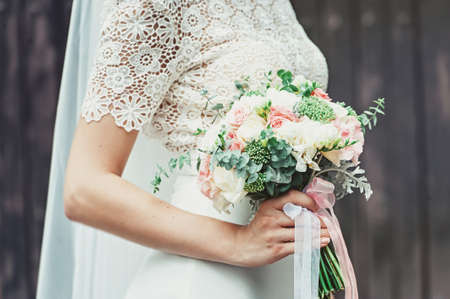 Beautiful young bride holds wedding bouquet of pastel beige tones roses in hands with french manicure. Closeup viewの写真素材