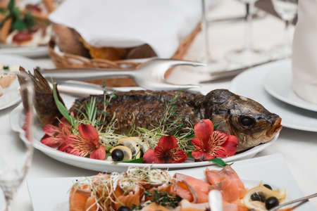 Stuffed fish in flowers, lemon, red pepper. Fragment of table setting.の写真素材
