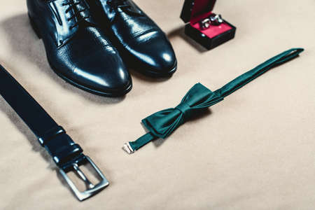 Closeup of elegant stylish black male accessories isolated on yellow fabric. High angle view of belt, shoes, cufflinks and green bow tie. Preparation for wedding concept.の写真素材
