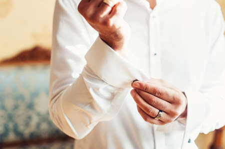 A man fastens black cufflink on the shirt. Close up of a man hand wearing a white shirt and cufflinks.の写真素材