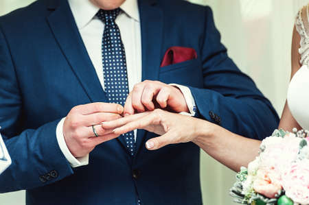 exchanging wedding rings. Groom puts a ring on the bride's finger. groom in a blue suit. The bride's bouquetの写真素材