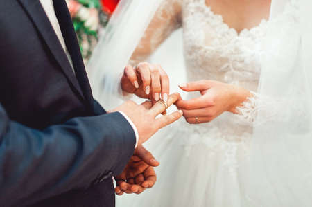 exchanging wedding rings. Bride puts a ring on the groom's finger. groom in a blue suit. The bride's bouquetの写真素材