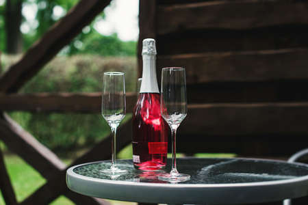 Two flute glasses and an pink champagne bottle with no label on a glass table in a back yard.の写真素材