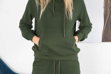 Stylish beautiful young blond woman in a green tracksuit poses near a white wall in the room.の写真素材