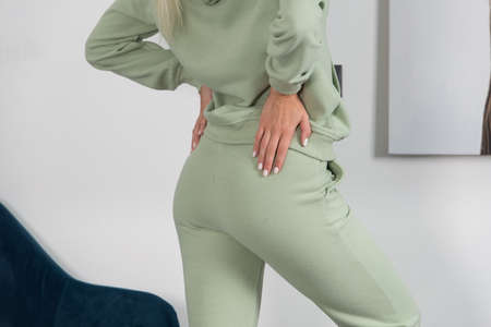 Stylish beautiful young blond woman in a green tracksuit poses near a white wall in the room.の写真素材