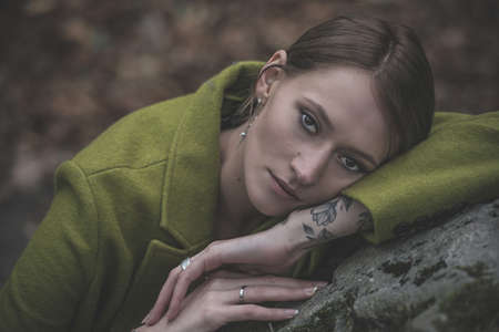 Fashionable young woman in green coat posing in a forest near the stone. Art portraitの写真素材