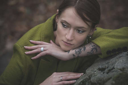Fashionable young woman in green coat posing in a forest near the stone. Art portraitの写真素材