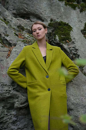 Fashionable young woman in green coat posing in a forest near the stone. Art portraitの写真素材