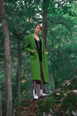 Fashionable young woman in green coat posing in a forest near the stone. Art portraitの写真素材