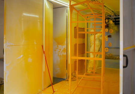 Construction worker in a protective suit spraying yellow paint to steel frame to prevent the rust on the surfaceの写真素材