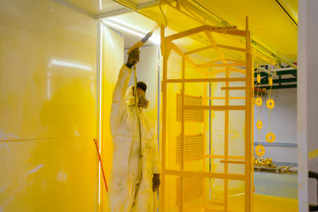 Construction worker in a protective suit spraying yellow paint to steel frame to prevent the rust on the surfaceの写真素材