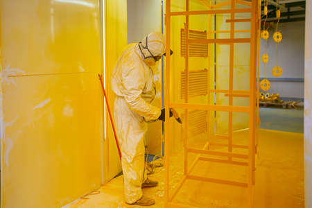 Construction worker in a protective suit spraying yellow paint to steel frame to prevent the rust on the surfaceの写真素材