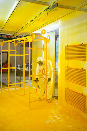 Construction worker in a protective suit spraying yellow paint to steel frame to prevent the rust on the surfaceの写真素材