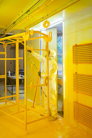Construction worker in a protective suit spraying yellow paint to steel frame to prevent the rust on the surfaceの写真素材