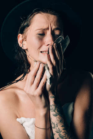 Beautiful woman in a towel and black hat holding dollars and worry for distress, crying angry and afraid. sad expression. Black backgroundの写真素材