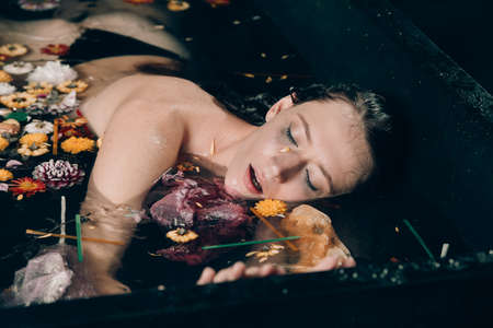 naked scared girl in the black bath full of garbage, environmental or polution concept.の写真素材