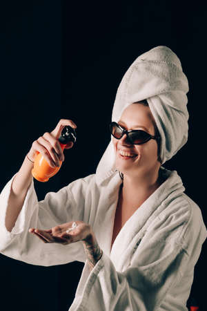 Skin Care, Woman in Sunglasses Applying Cream in Bath Towel after Spa, Treatment Cosmetic Moisturizing Lotion. Black backgroundの写真素材