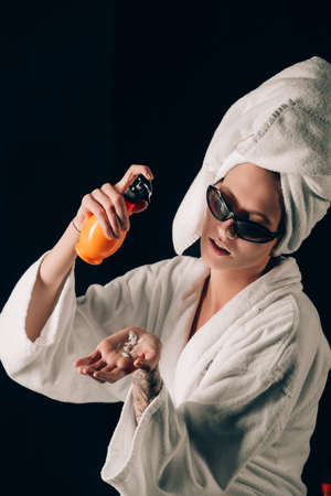 Skin Care, Woman in Sunglasses Applying Cream in Bath Towel after Spa, Treatment Cosmetic Moisturizing Lotion. Black backgroundの写真素材