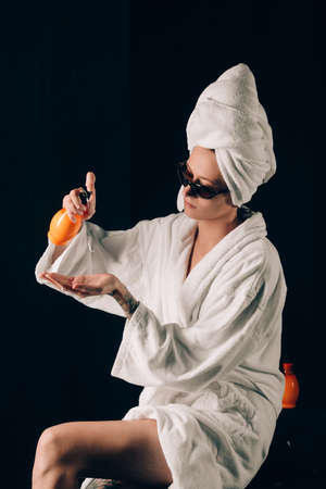 Skin Care, Woman in Sunglasses Sitting on the Edge of Black Bath Applying Cream in Towel after Spa, Treatment Cosmetic Moisturizing Lotion. Black backgroundの写真素材