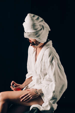 Skin Care, Woman in Sunglasses Sitting on the Edge of Black Bath Applying Cream in Towel after Spa, Treatment Cosmetic Moisturizing Lotion. Black backgroundの写真素材