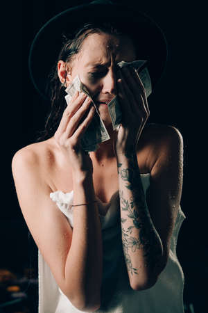 Beautiful woman in a towel and black hat holding dollars and worry for distress, crying angry and afraid. sad expression. Black backgroundの写真素材