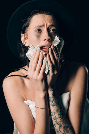 Beautiful woman in a towel and black hat holding dollars and worry for distress, crying angry and afraid. sad expression. Black backgroundの写真素材